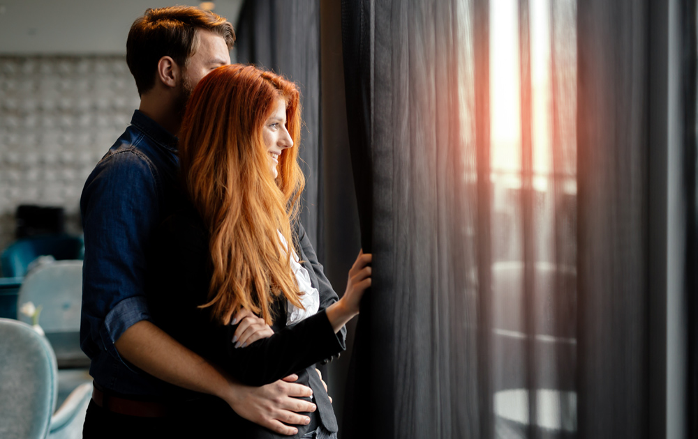 A couple looking out of a hotel room at a sunset