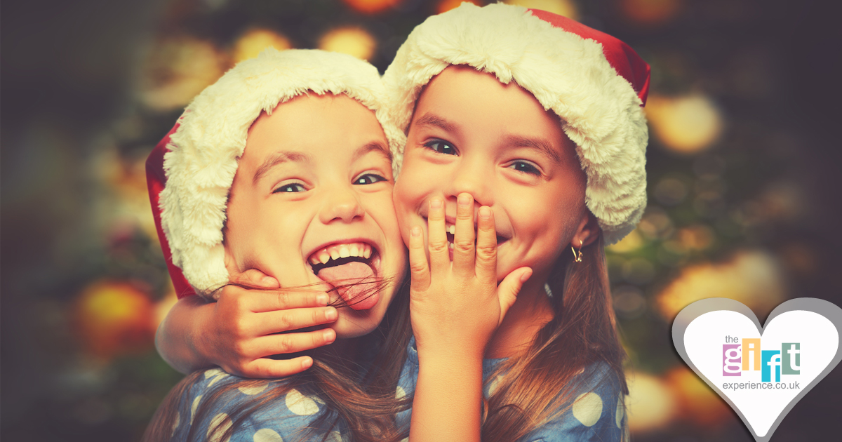 Two children in santa hats in front of a Christmas tree