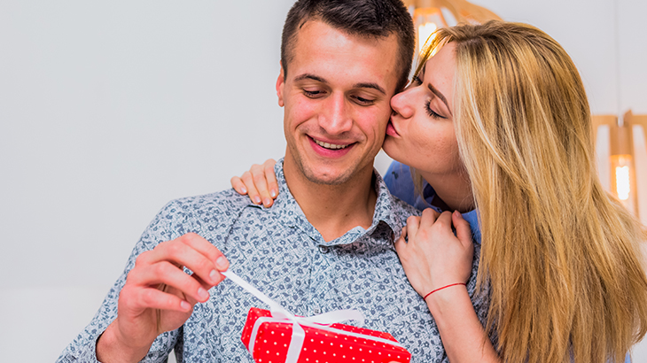 Wife kissing husband on the cheek as he opens a thoughtful anniversary gift, celebrating love and special moments