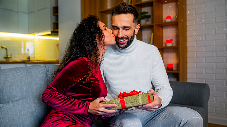 Wife giving husband a thoughtful anniversary gift and a kiss on the cheek, celebrating love and special moments