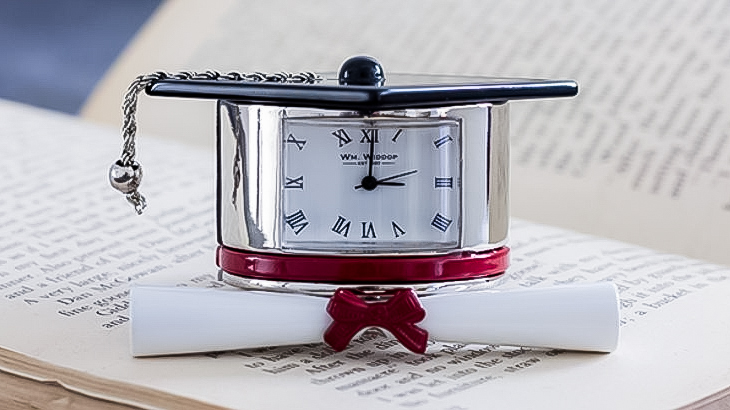 Graduation mortar board cap with diploma scroll and mini clock on open book symbolising education, academic achievement, and time management