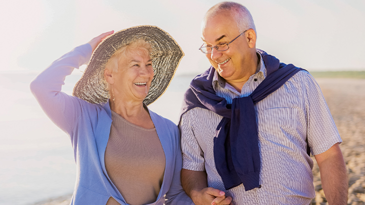 Senior couple walking on the beach laughing together during 50th wedding anniversary celebration