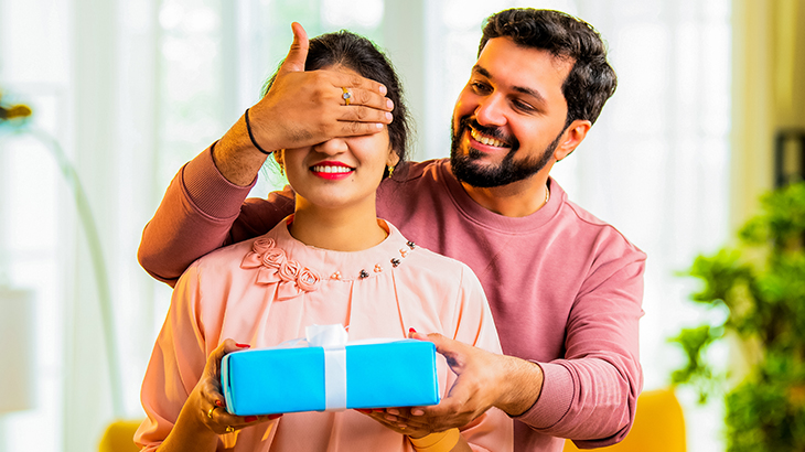 Husband surprising wife by covering her eyes and presenting a thoughtful anniversary gift, celebrating love and special moments