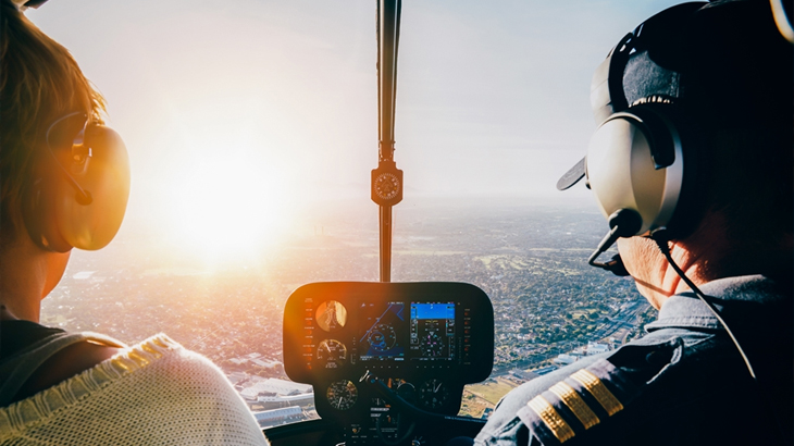 Helicopter pilot and passenger looking out at scenic landscape below, aerial sightseeing tour, helicopter ride experience