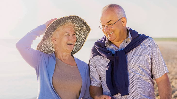 Senior couple walking along the beach laughing together during a romantic getaway gift experience, perfect for anniversaries and special occasions