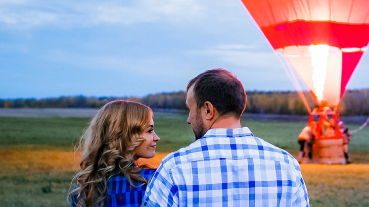 Romantic couple looking at each other with hot air balloon in background, adventure date experience, hot air balloon ride for couples