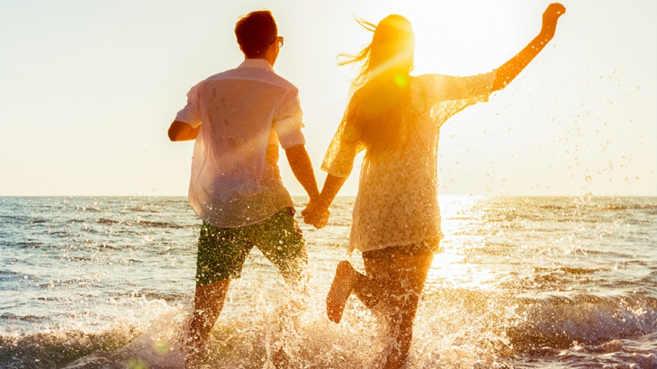 Couple running hand in hand through the sea during a romantic getaway gift experience, perfect for anniversaries and special celebrations
