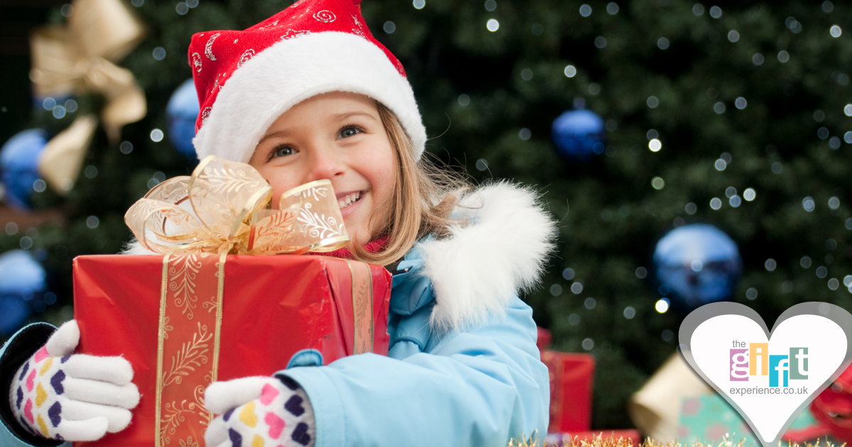 Little girl in a Santa hat holding a gift by the Christmas Tree