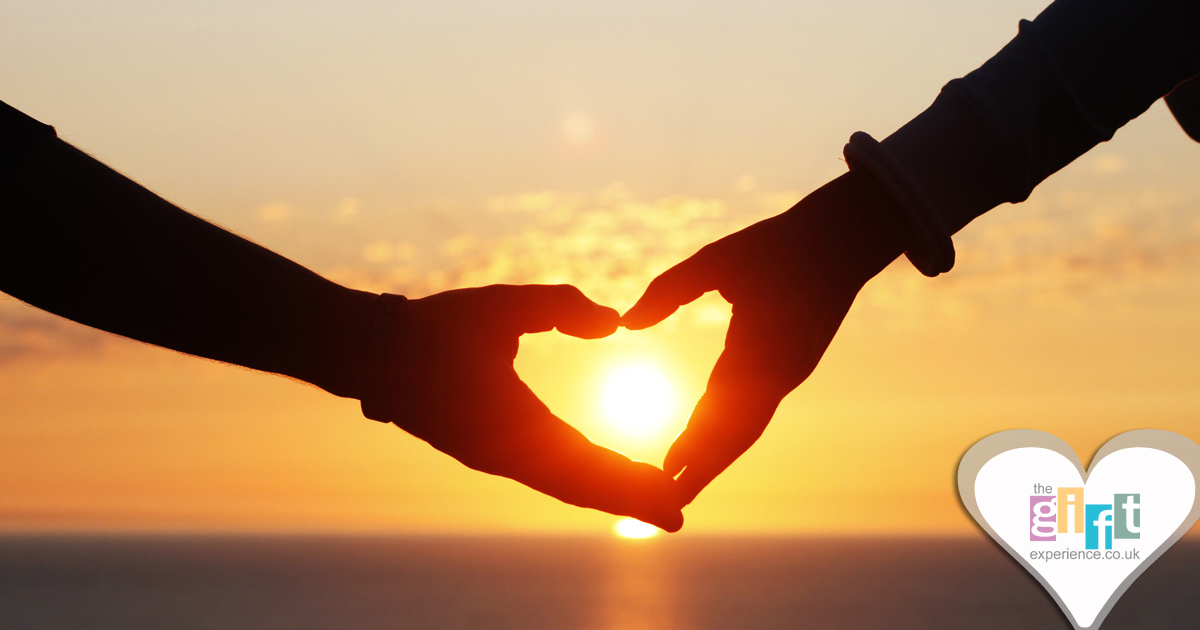 couple at sunset making a hreat with their hands